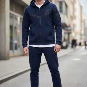 Чоловічий спортивний костюм Nike Dri-FIT сірого кольору, що складається зі штанів та кофти на блискавці, на моделі під час активного відпочинку на вулиці.